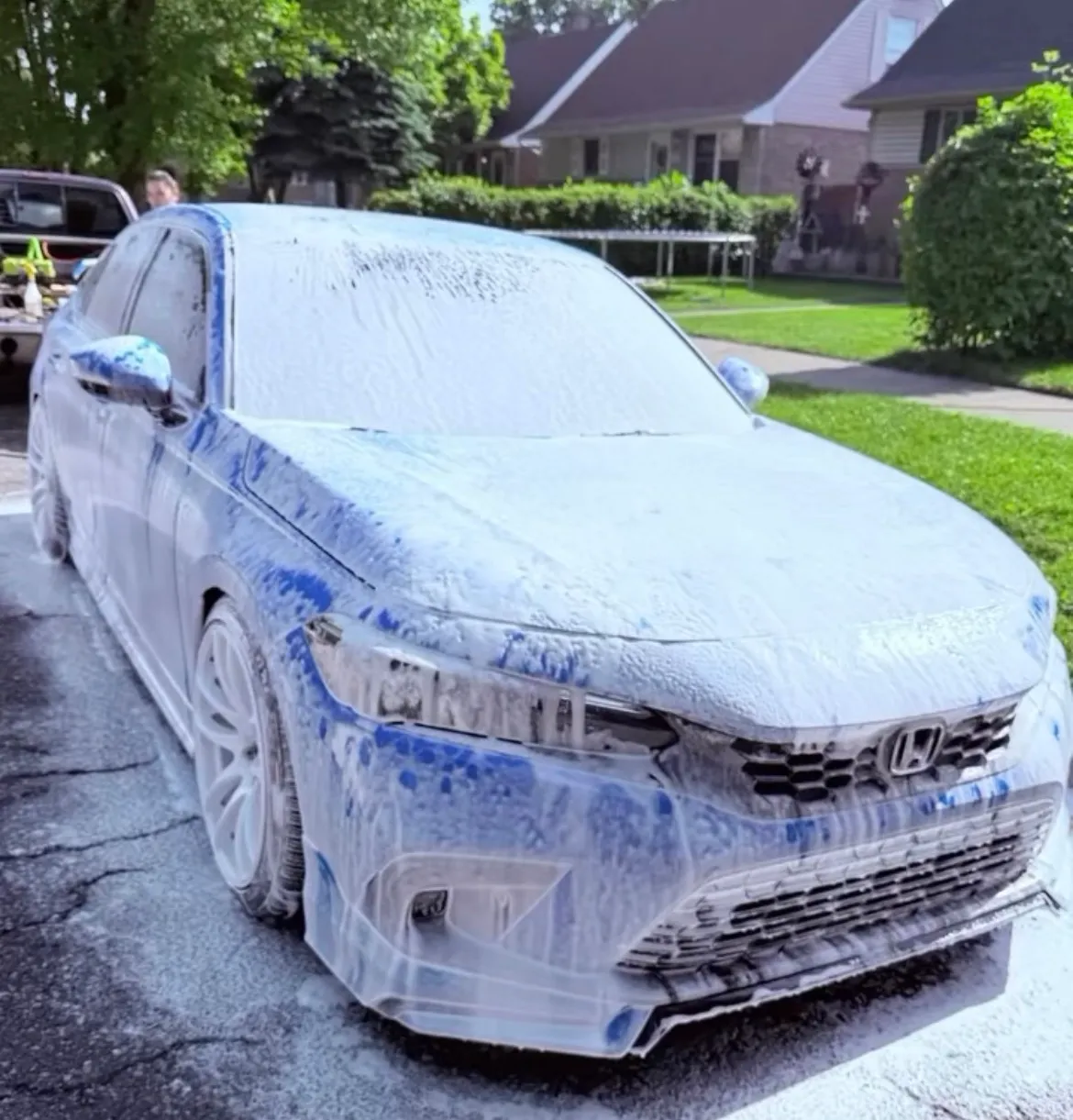 A Honda Civic coated in snow foam in a driveway during the pre-wash stage of an exterior detail.